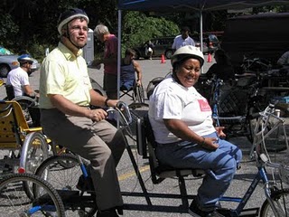 Photo of a tricycle built for two with smiling occupants in helmets. 