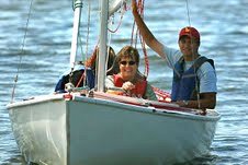 Gigi Ranno and two others sailing. Ranno is smiling, with one hand on the tiller. 