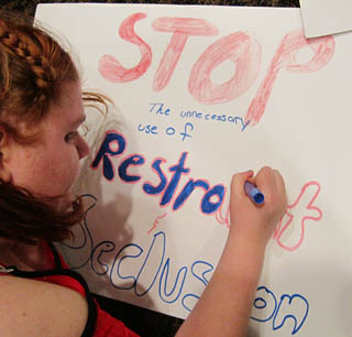 Girl draws poster that says stop the unnecessary use of restraint and seclusion 