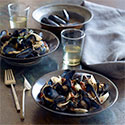 Bowls of mussels on a table set with water glasses and a linen napkin.