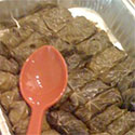 Tray of wrapped grape leaves with an orange serving spoon.