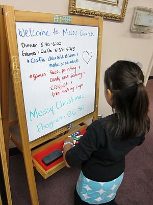 Girl reading a welcome board about Messy Church