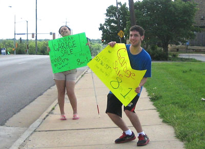 Youth waving garage sale signs on sidewalk near street