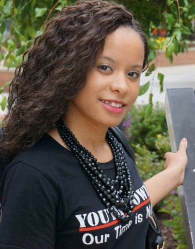 Pauline with long flowing hair, beaded black neckllace and YOUTH POWER! Our Time is Now shirt