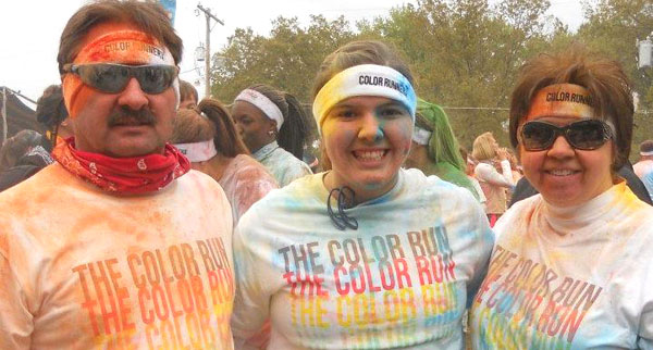 Rachel stands, covered in multiple colors, with her parents at a 5K race